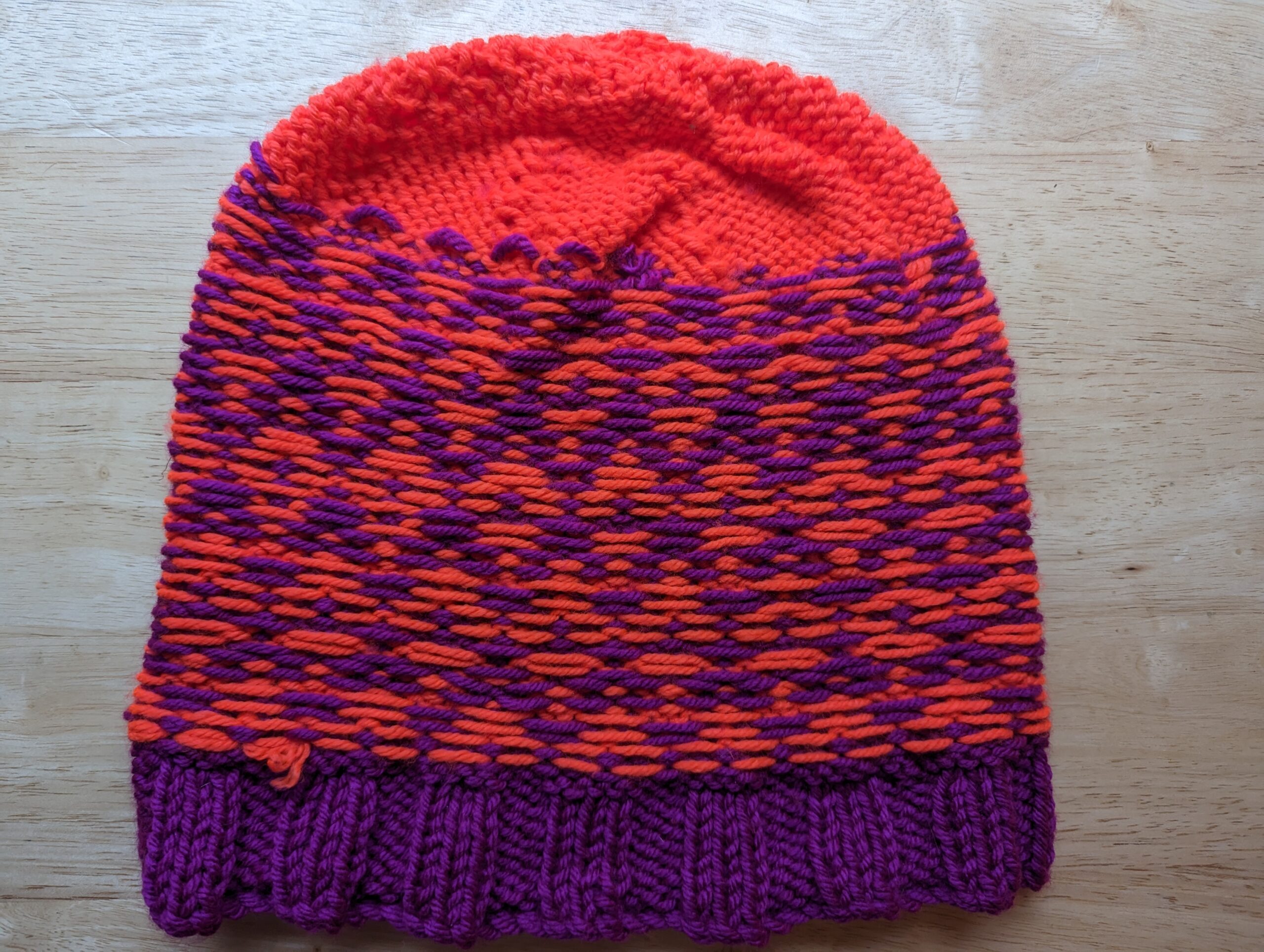 The inside of a colorwork hat in violet and neon orange with a diamond pattern showing very clean floats. The rim is violet and the crown is orange.