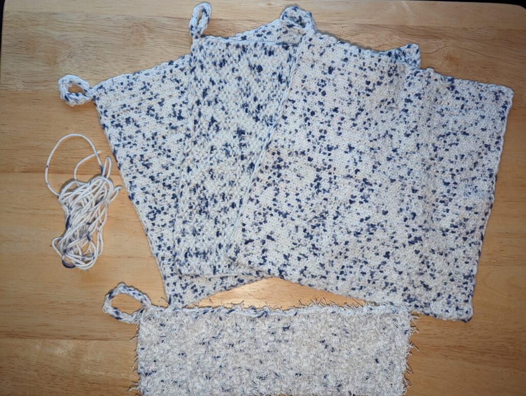 Three 8" by 8" wash cloths that are mostly white with occasional indigo blue specks, there is also a smaller (8" x 2") scrubber that is "fluffier" as it has the cotton/linen blend yarn mixed with white polyester eyelash yarn.